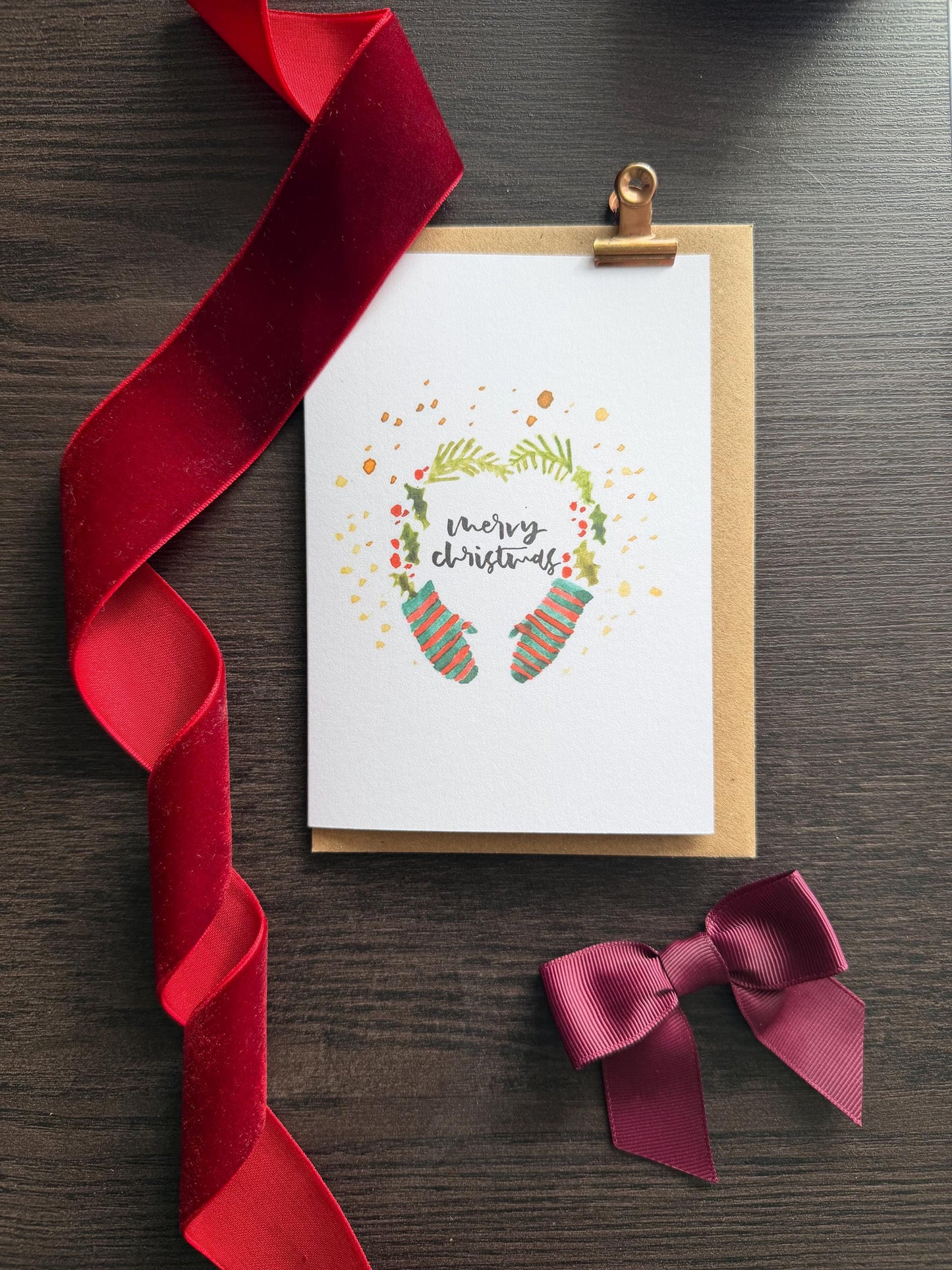 Christmas card with festive design, red ribbon, and bow on a wooden surface