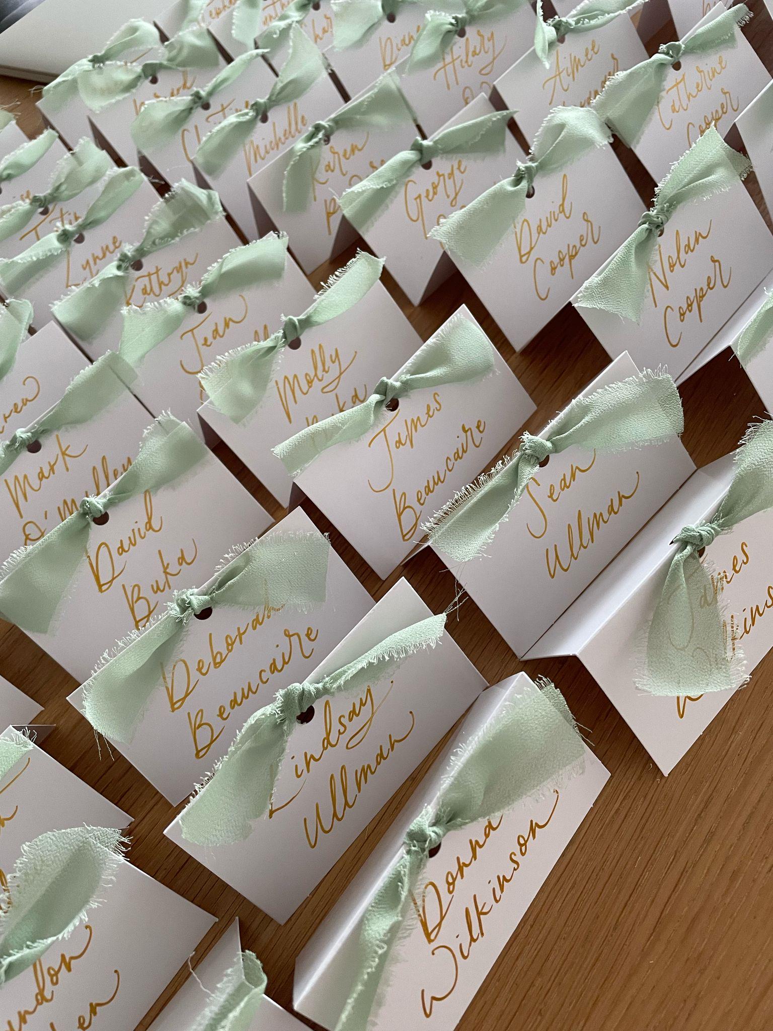 Small boxes with green ribbons and personalized names on a wooden surface