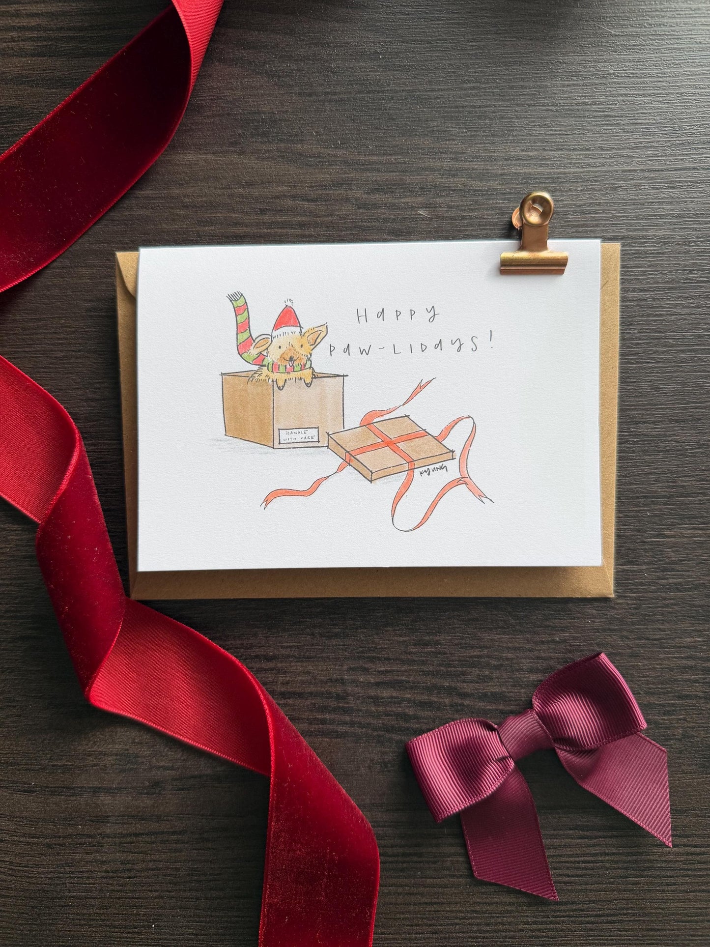 Greeting card with a cat illustration and red ribbon on a wooden surface