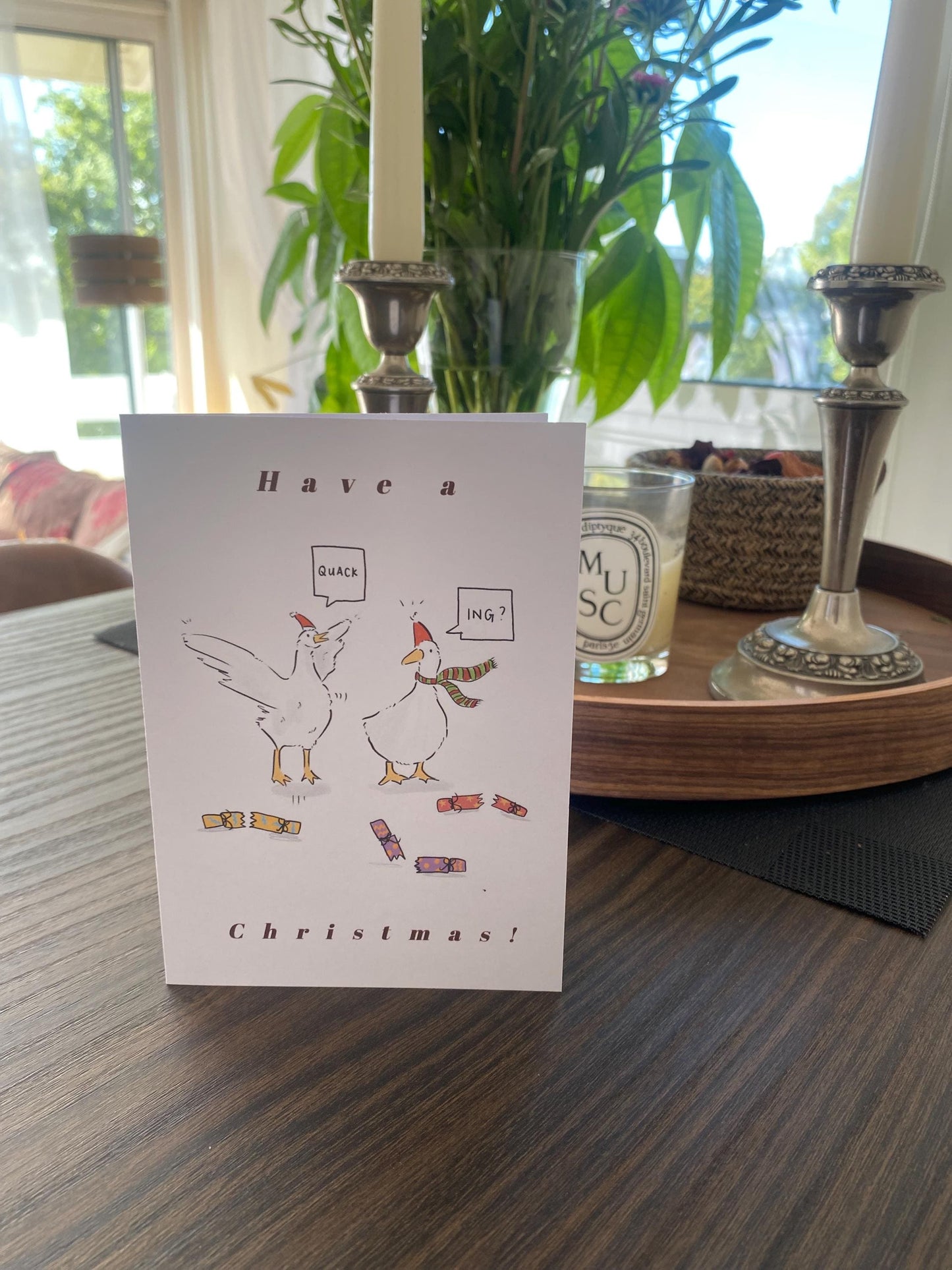 Christmas card with cartoon hens on a table with candles and plants in the background