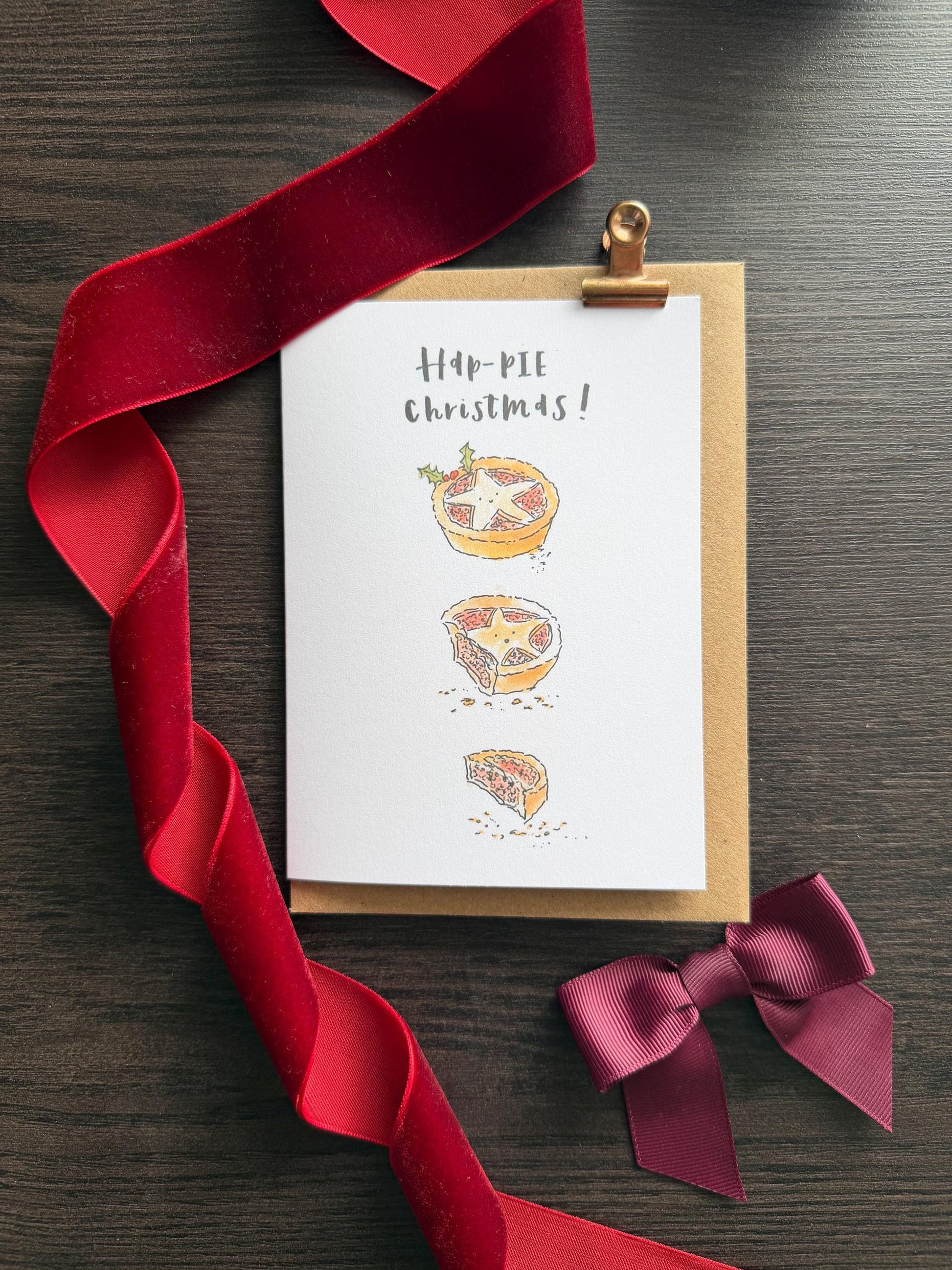 Greeting card with pie illustrations and red ribbon on a wooden surface
