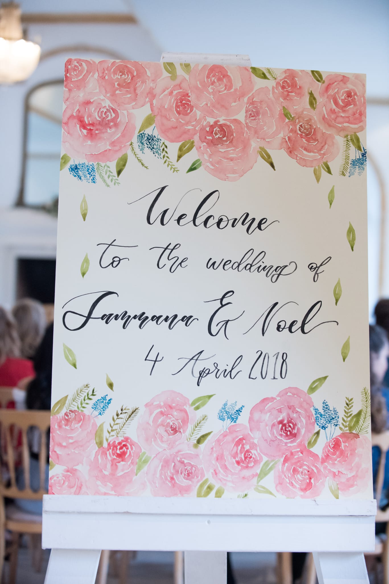 Wedding welcome sign with floral design and text on a stand.