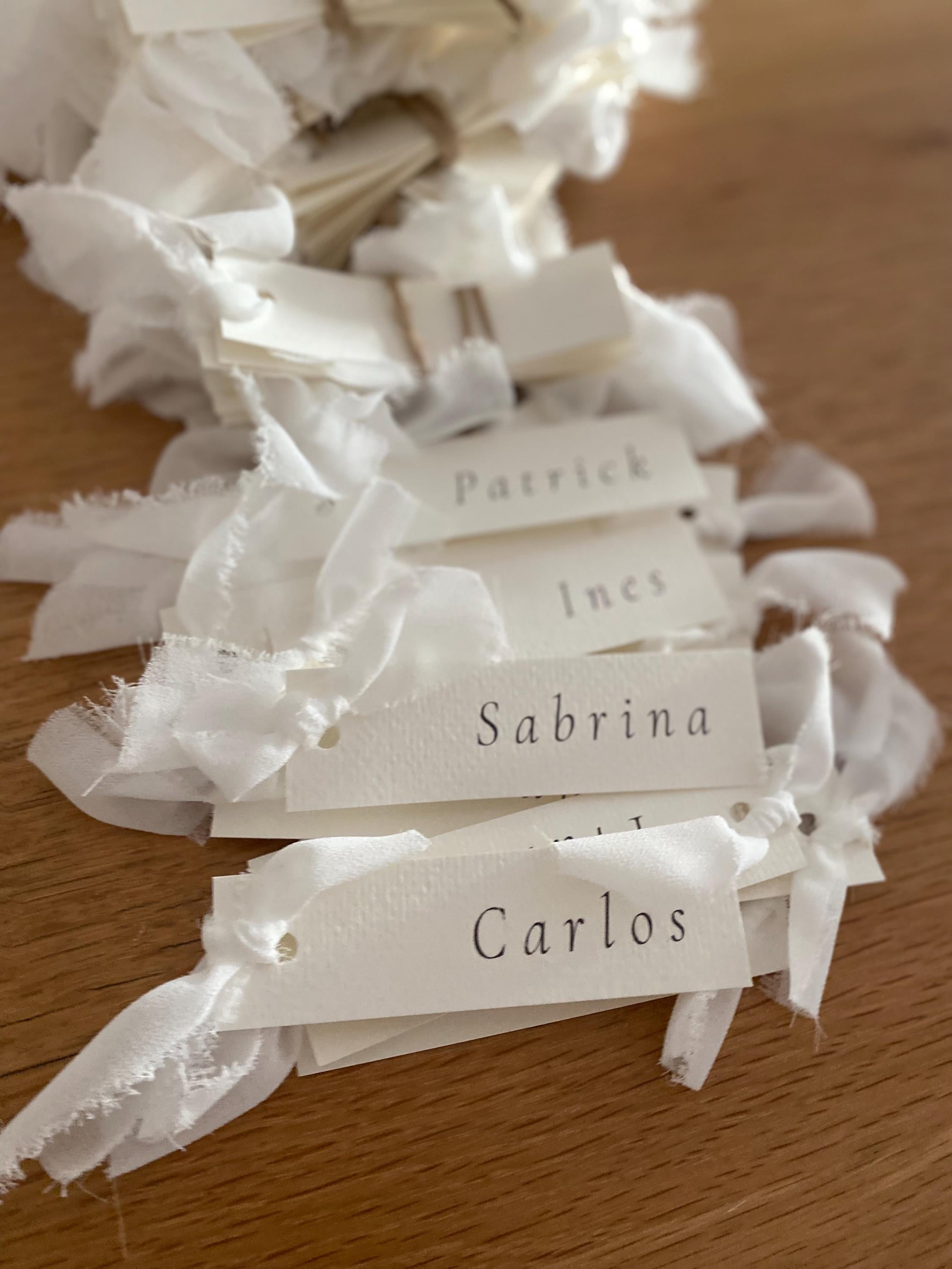 White name tags on ribbons with names Patrick, Ines, Sabrina, and Carlos on a wooden surface.