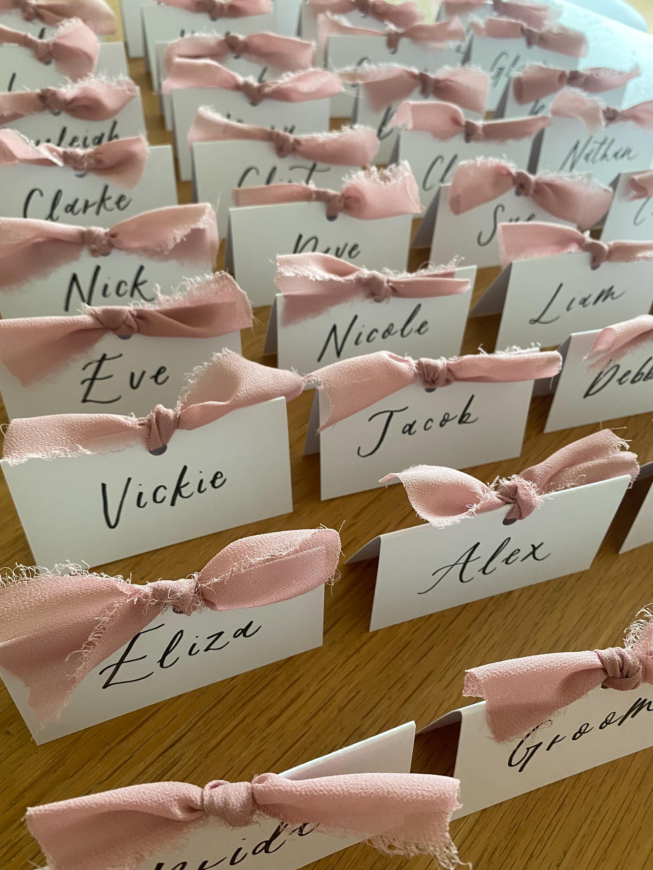 Place cards with pink ribbons arranged on a wooden surface