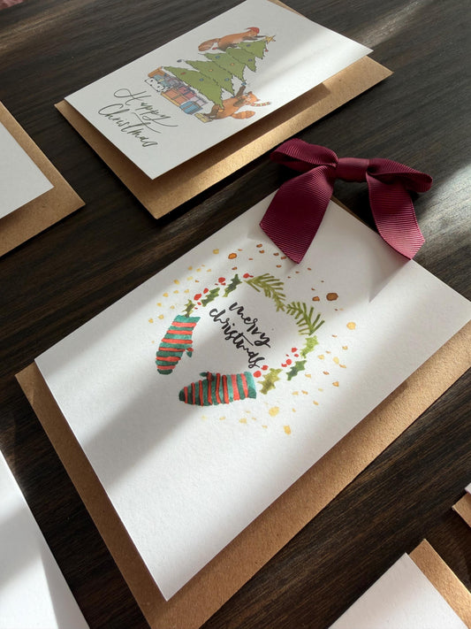 Christmas-themed greeting card with stockings and wreath on a wooden surface