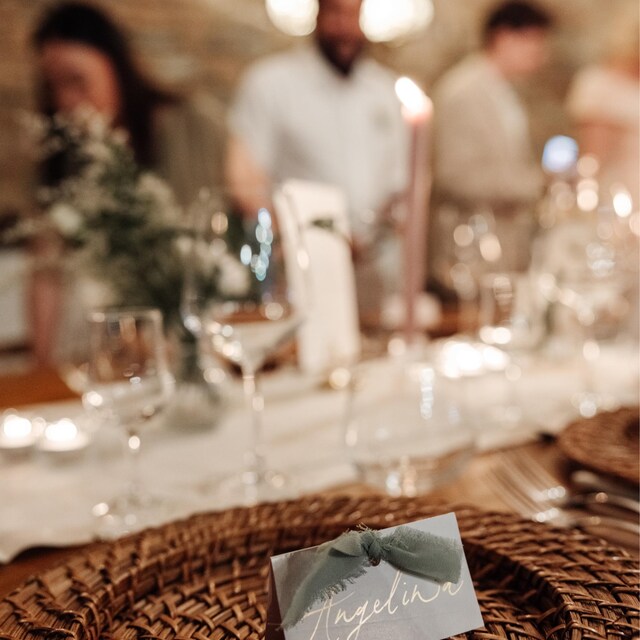 Table setting with a name card on a woven placemat, blurred background of people and decor.