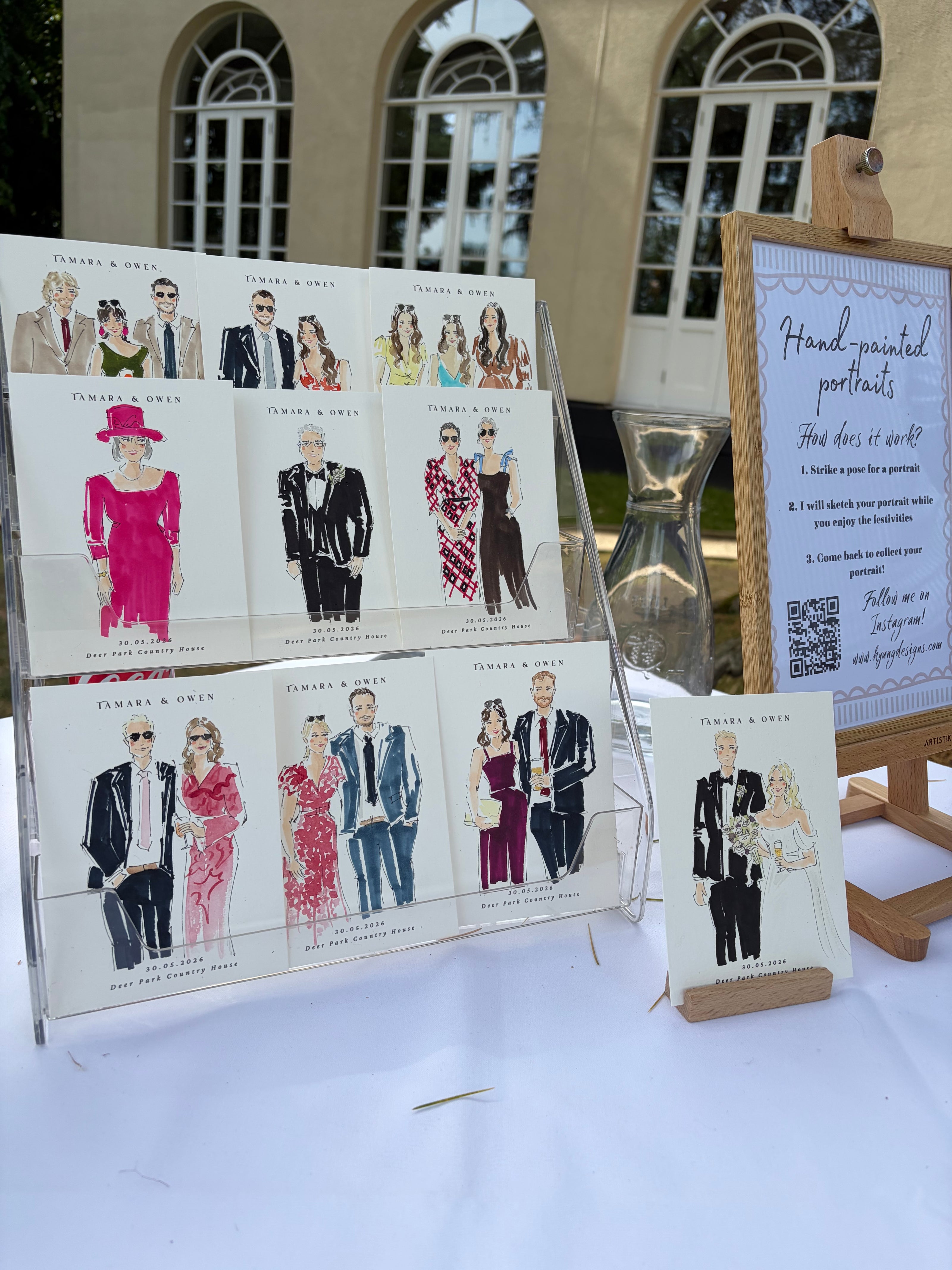 Live illustration artistic portraits of couples displayed outdoors with a sand timer and sign.