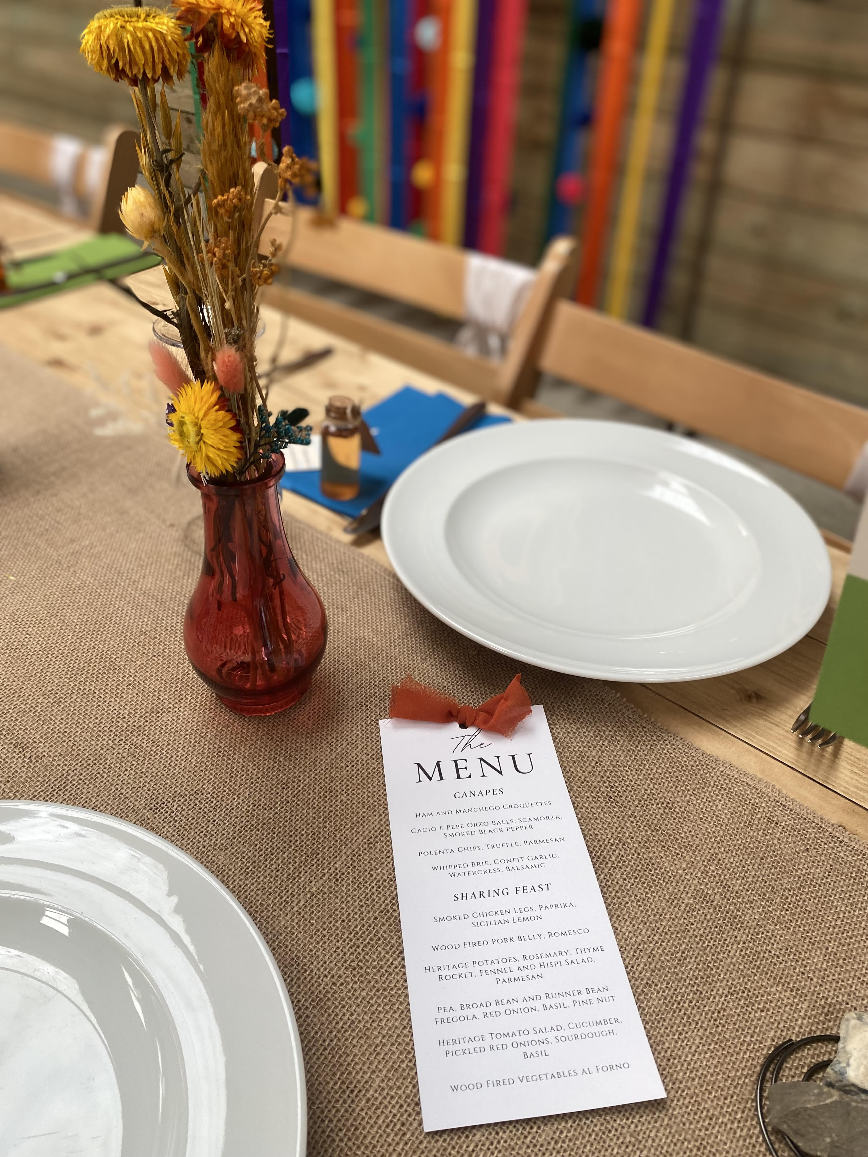 Table setting with plates, a vase of flowers, and a menu on a tablecloth.